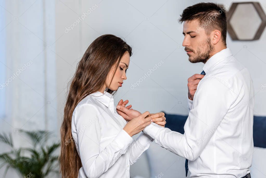 Side view of girlfriend buttoning boyfriend cuff in morning at home, sexism concept