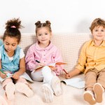 Lindos niños felices sentados en el sofá y aprendiendo juntos