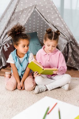 çok güzel çok ırklı çocuklar halı üzerinde oturan ve birlikte kitap okuma 