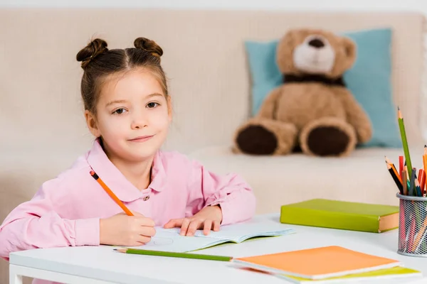 Lindo Niño Escribiendo Con Lápiz Sonriendo Cámara Mientras Estudia Casa —  Fotos de Stock