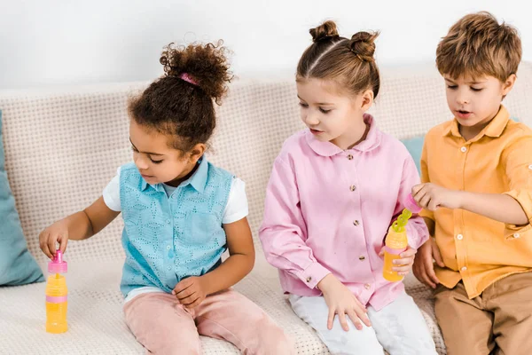 Adorable Multiethnic Children Sitting Sofa Blowing Soap Bubbles — Free Stock Photo
