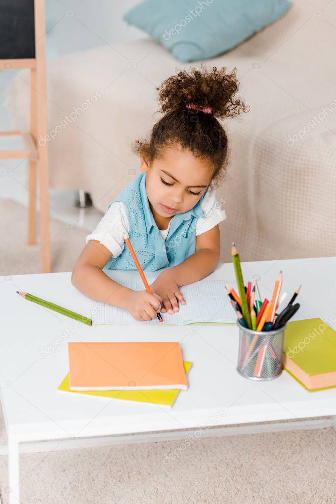 high angle view of cute african american child sitting and writing with pencil