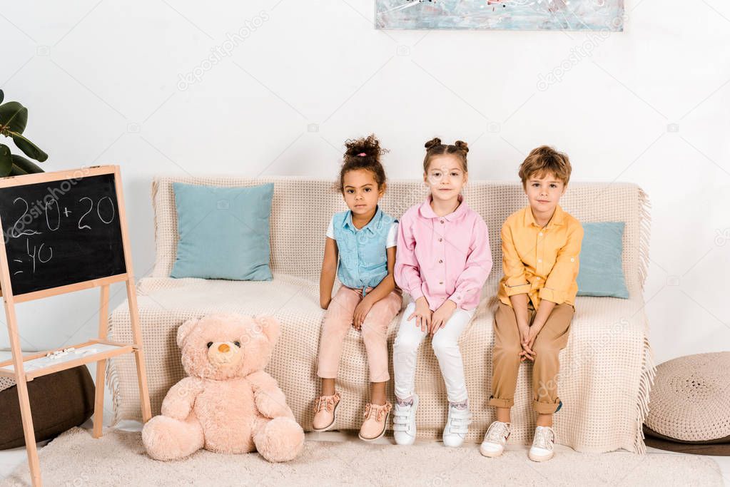 beautiful multiethnic children sitting on couch and looking at camera 