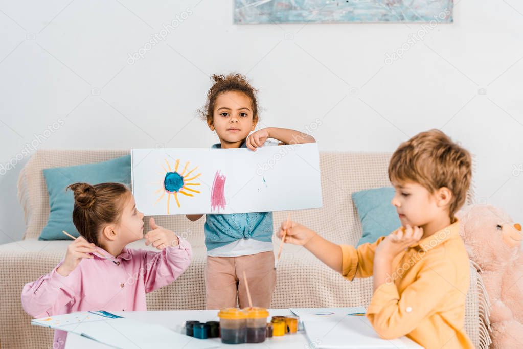cute african american child showing picture while painting with friends