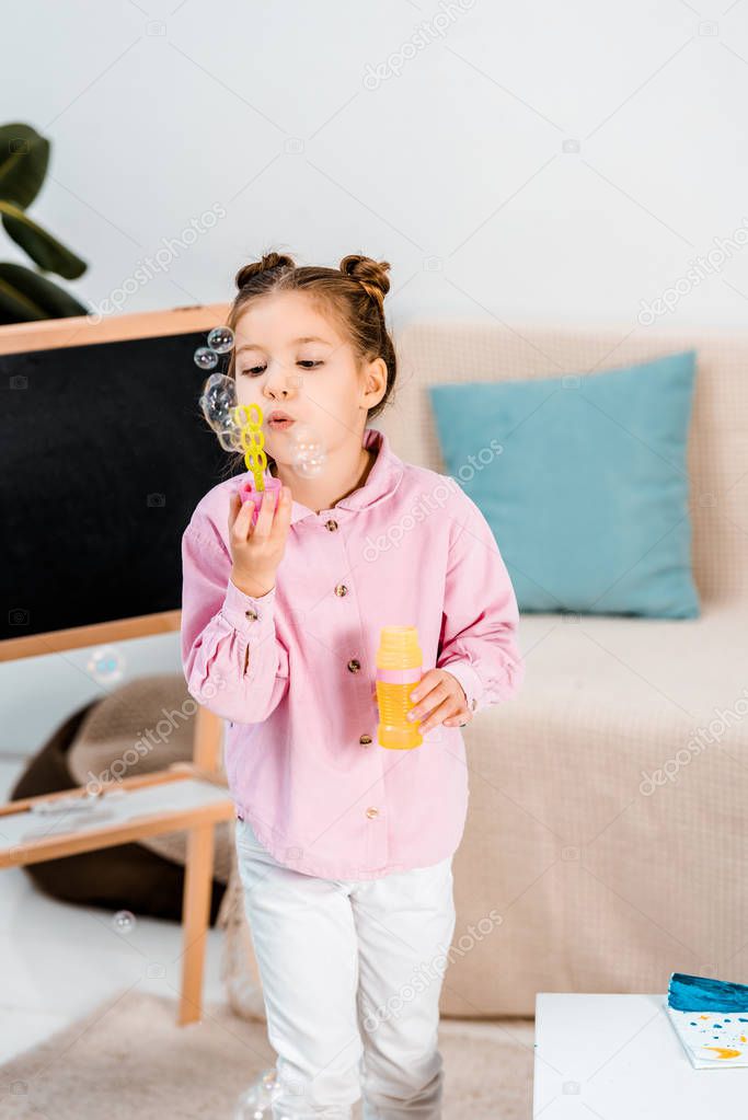 beautiful child standing near blackboard and blowing soap bubbles 