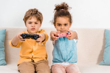 Çok güzel çok ırklı çocuklar oyun çubukları ile bilgisayar oyunu oynamak ve kameraya bakıyor