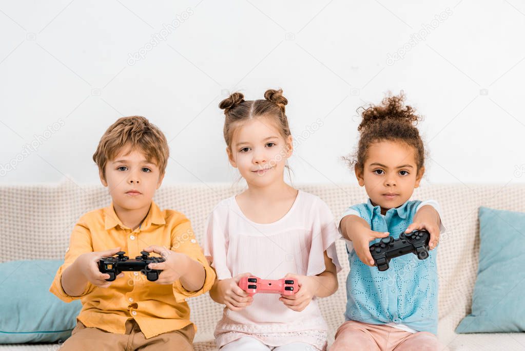 Cute little kids playing video game with joysticks and looking at camera