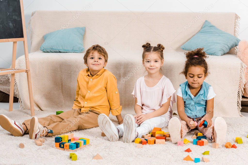 adorable multiethnic kids playing with colorful cubes and smiling at camera 