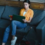 Beautiful mixed race girl in orange shirt choosing vinyl on sofa in living room