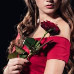 Partial view of woman in red dress holding rose isolated on black