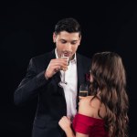 Joven pareja en formal desgaste beber champán aislado en negro