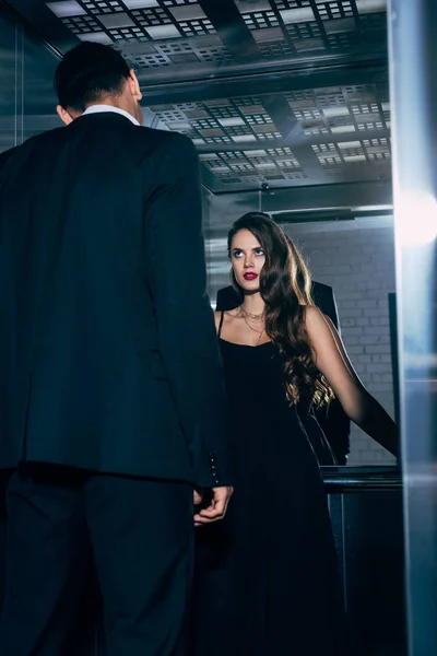 美丽的女人在黑色礼服热情地看着男人在电梯里 — 图库照片
