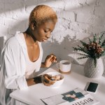 Schöne afrikanisch-amerikanische Frau beim Frühstück in der weißen Küche Schöne afrikanisch-amerikanische Frau beim Frühstück in der weißen Küche