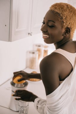 cheerful african american woman preparing squeezing orange  clipart