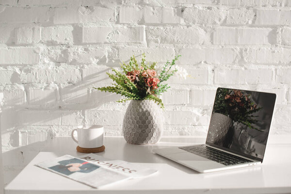 laptop with blank screen in white kitchen near business newspaper