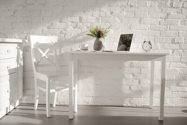 laptop in white kitchen near cup and vase with flowers in kitchen 