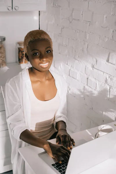 Улыбающаяся Африканская Американка Печатающая Ноутбуке Белой Кухне — Бесплатное стоковое фото