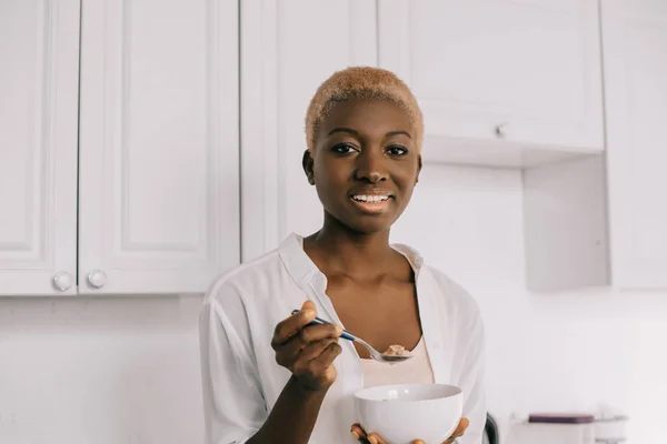 happy african american woman holding spoon and bowl with cornflakes