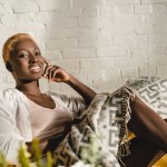 Sarı kanepe battaniyenin altında yatan neşeli Afrikalı-Amerikalı kadın