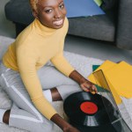 Mujer afroamericana con pelo corto sosteniendo disco de vinilo cerca de tocadiscos