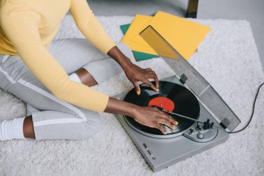 cropped view of african american woman using record player on carpet clipart