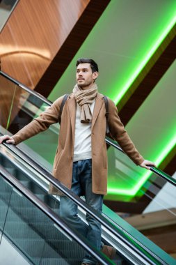 yakışıklı adam sıcak giyim alışveriş alışveriş merkezinde yürüyen merdiven iniyor