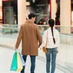 Achteraanzicht van een liefdevol paar met boodschappentassen hand in hand in winkelcentrum