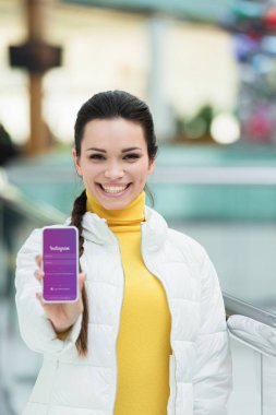 gülümseyen, kameraya bakıyor ve smartphone ekran instagram cihaz ile gösterilen güzel kız