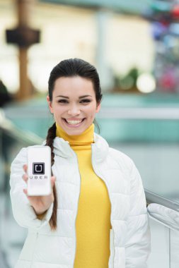 smiling girl looking at camera and showing smartphone screen with uber app clipart