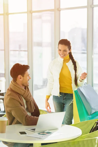 Beautiful Girl Shopping Bags Looking Man Sitting Table Laptop Cafe — Free Stock Photo