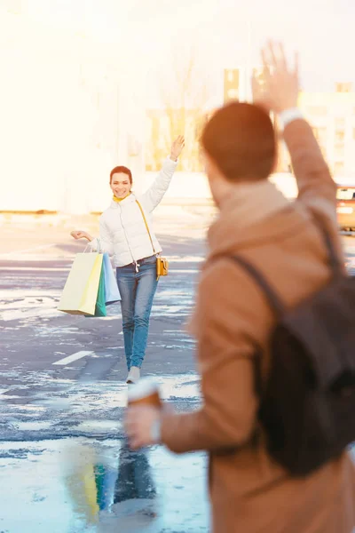 Attraktiva Flicka Med Shoppingkassar Viftande Med Handen Till Pojkvän Parkering — Gratis stockfoto