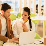 Handsome man typing on laptop keyboard and worried girl looking at screen in cafe