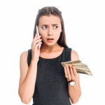 Retrato de mujer de negocios emocional con billetes de dólar hablando en un teléfono inteligente aislado en blanco