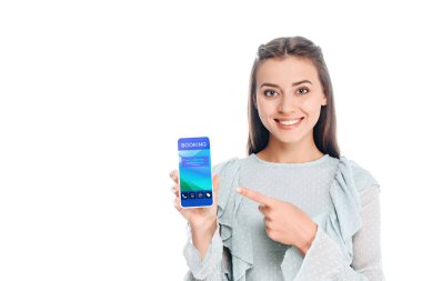 smiling woman showing smartphone with booking lettering isolated on white