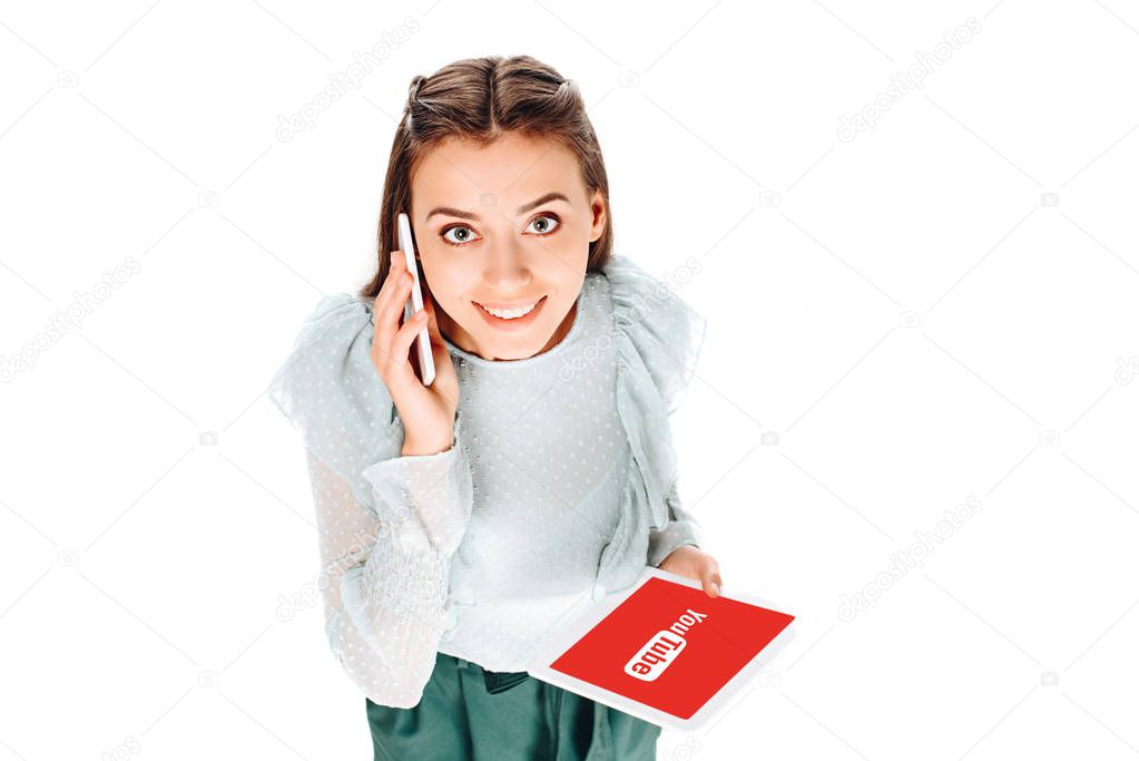 High angle view of smiling woman with tablet talking on smartphone isolated on white