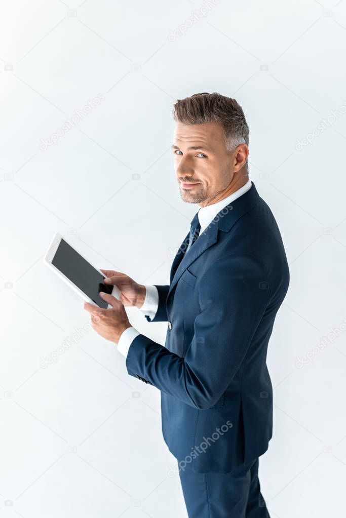 high angle view of handsome businessman holding tablet with blank screen and looking at camera isolated on white