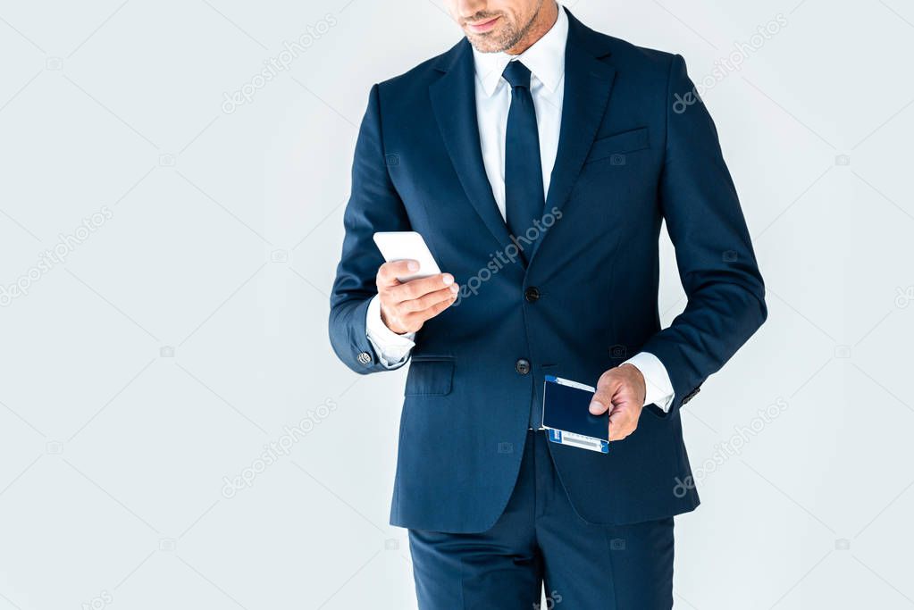 cropped image of businessman using smartphone and holding passport with ticket isolated on white