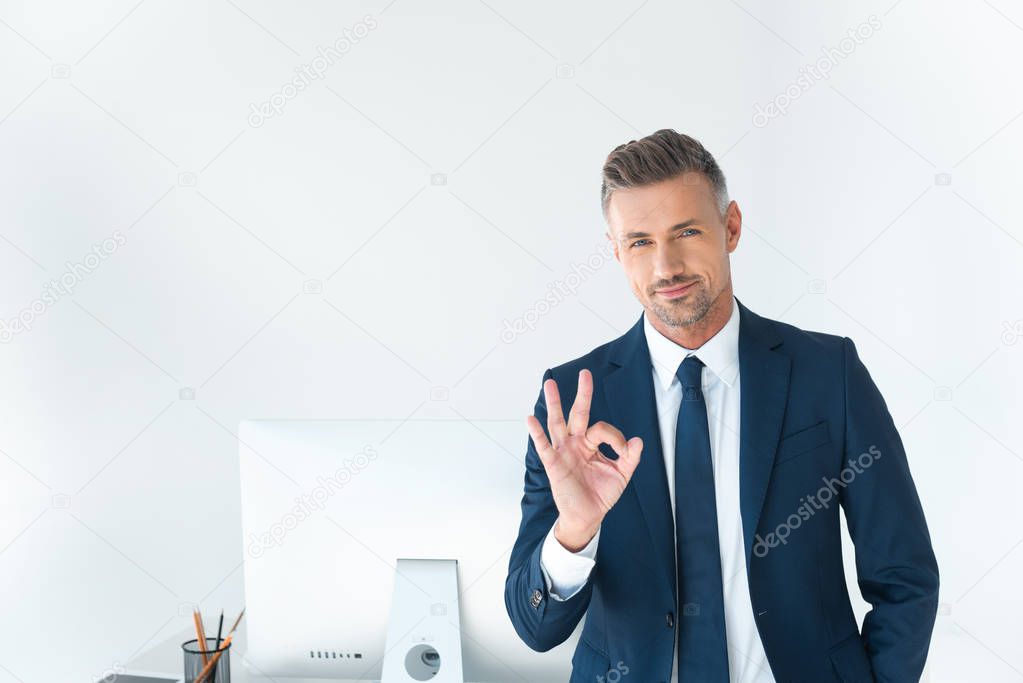 handsome businessman showing okay gesture and looking at camera isolated on white
