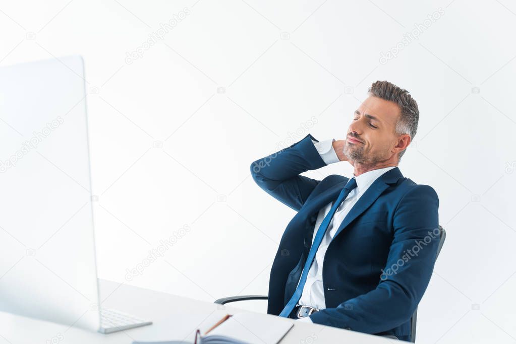 cheerful tired businessman touching neck and sitting on chair isolated on white