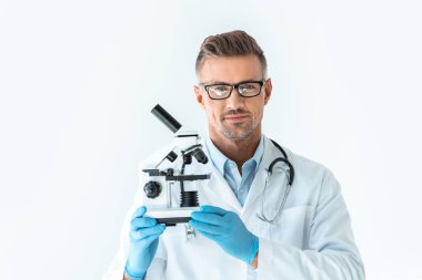 handsome scientist in glasses holding microscope and looking at camera isolated on white clipart