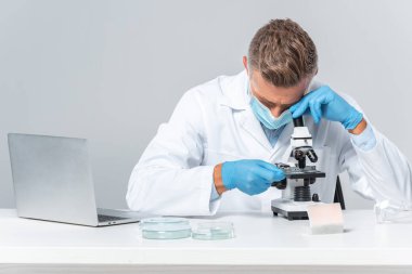 Tıbbi maskesi ve Medikal Ürünler üzerinde beyaz izole mikroskop bakarak yakışıklı bilim adamı