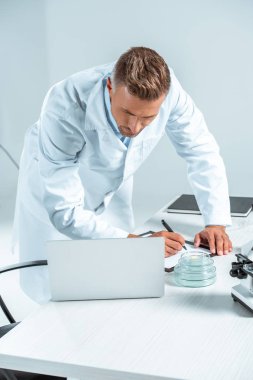 bir şey yazma ve dizüstü bilgisayar üzerinde beyaz izole bakarak yakışıklı bilim adamı
