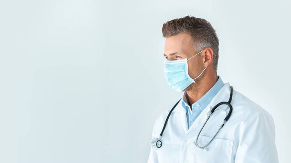 handsome doctor in medical mask looking away isolated on white