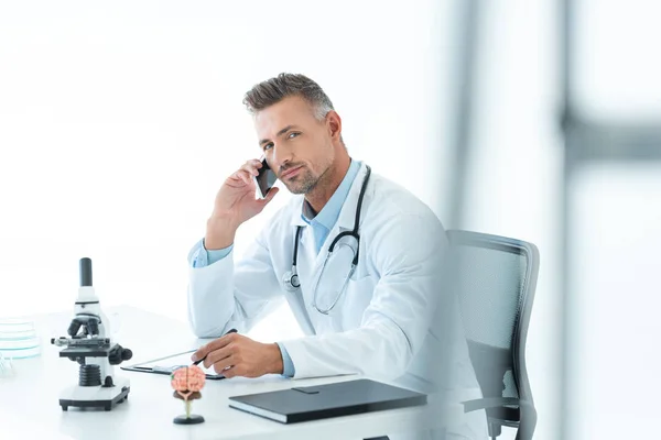 Handsome Scientist Talking Smartphone Table Looking Camera Isolated White — Free Stock Photo