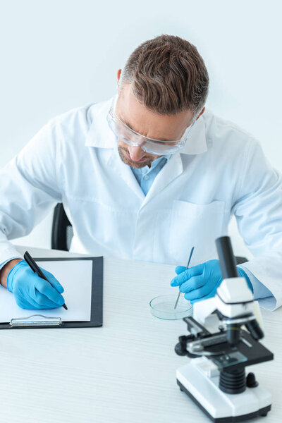 handsome scientist in protective glasses writing about experiment isolated on white