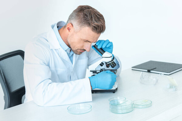 handsome chemist making test with microscope isolated on white