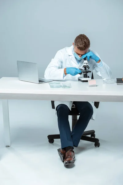 Kimiawan Tampan Bertopeng Medis Dan Sarung Tangan Medis Melihat Mikroskop — Foto Stok Gratis