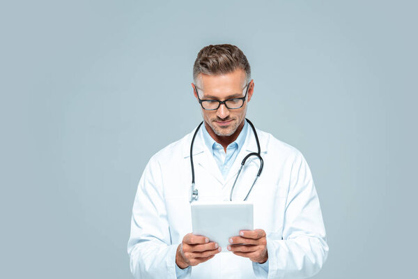 handsome doctor with stethoscope looking at tablet isolated on white