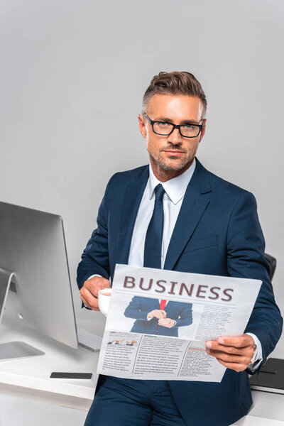 красивый бизнесмен держит чашку кофе и деловую газету изолированы на белом, глядя в камеру
