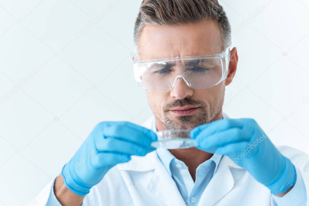 portrait of handsome scientist in protective glasses looking at reagent during experiment isolated on white